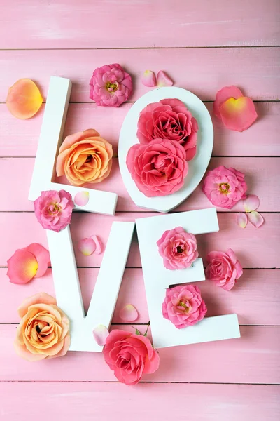 Beautiful roses with word LOVE on pink wooden planks background — Stock Photo, Image
