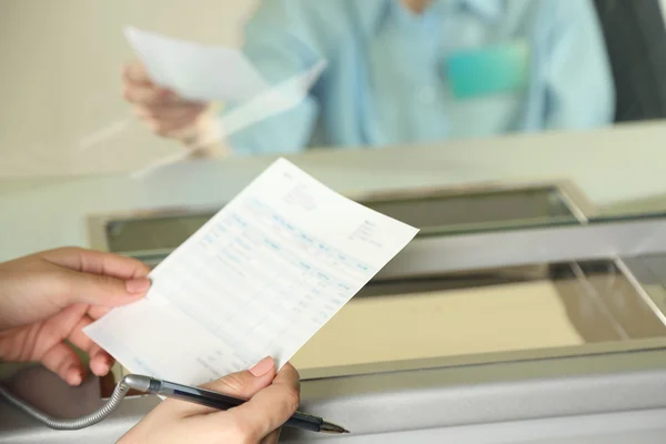 Geldausgabefenster mit arbeitender Kassiererin und weibliche Hände mit Anspruchsprüfung. Konzept der Bezahlung von Versorgungsunternehmen — Stockfoto