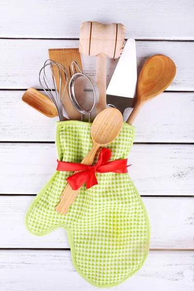 Set of kitchen utensils in mitten on wooden background — Stock Photo, Image