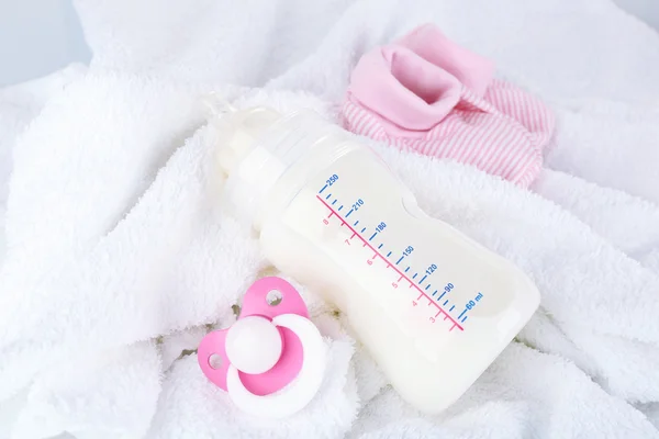 Dětské mléko láhev, dudlík a babys bootees na ručník — Stock fotografie