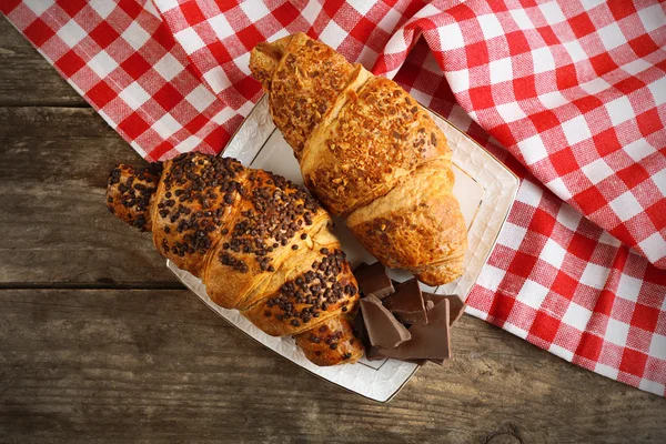 Croissants frescos e saborosos com chocolate na placa, no fundo de madeira — Fotografia de Stock