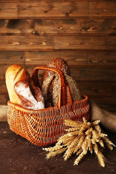 Pane diverso con orecchie in cesto su sfondo di legno — Foto Stock