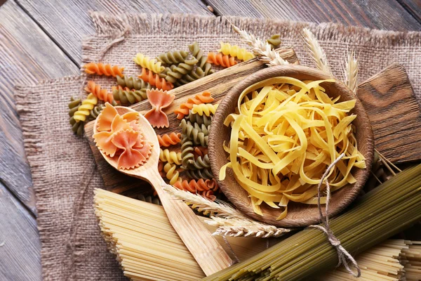 Verschillende soorten pasta op zak op houten achtergrond — Stockfoto