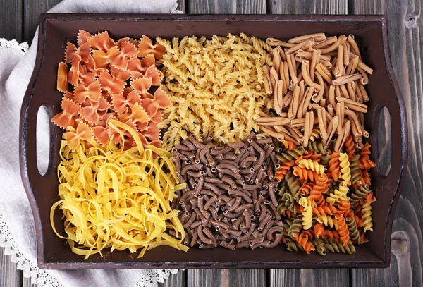 Verschiedene Arten von Pasta in Tablett auf Holzgrund — Stockfoto
