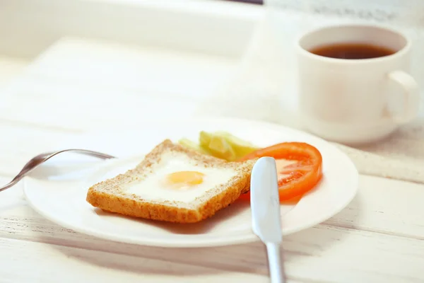 Rührei mit Brot auf Teller mit Tasse Tee auf hellem Hintergrund — Stockfoto