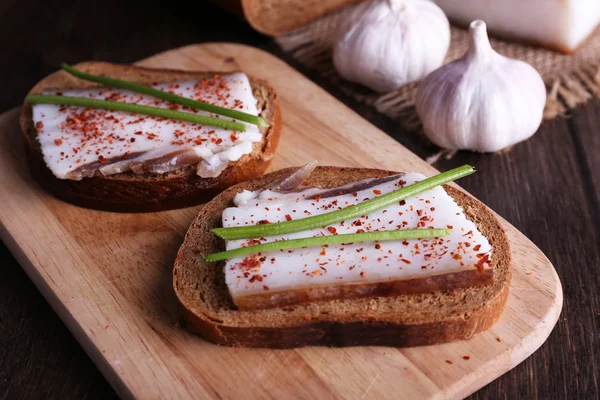 Sandwiches with lard on cutting board and garlic on table close up — Stock Photo, Image