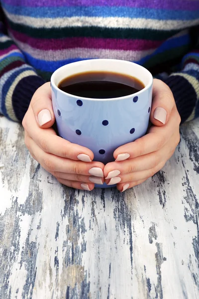 Vrouwelijke handen met kopje koffie op houten tafel close-up — Stockfoto