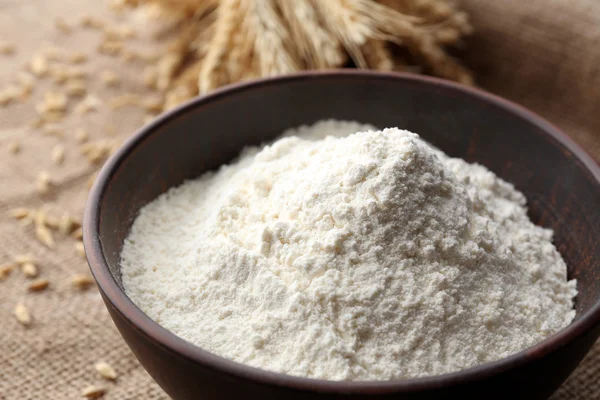 Flour in bowl with ears and grains on sackcloth background — Stock Photo, Image