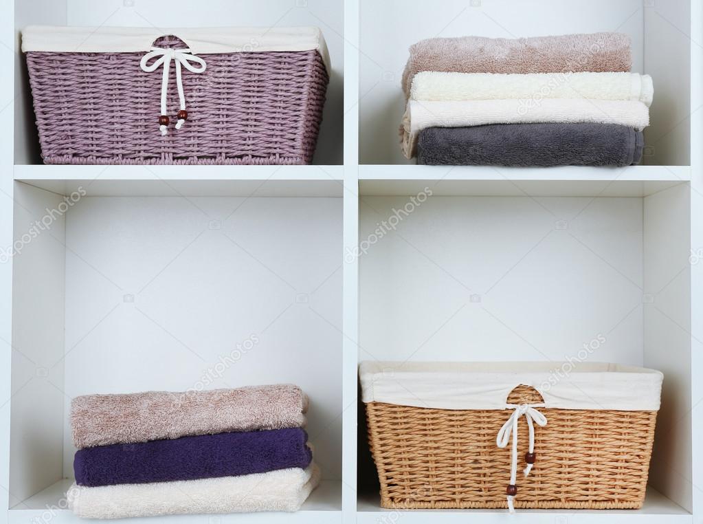 Colorful towels with wicker baskets on shelf of rack background