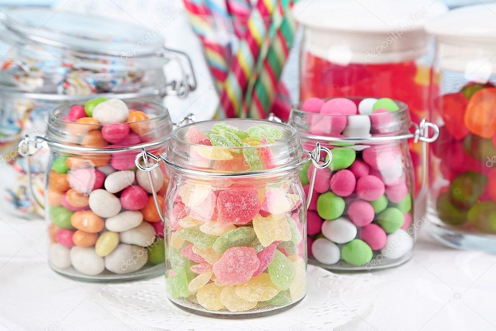 Multicolor candies in glass jars on color wooden background
