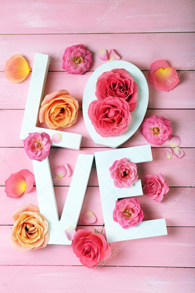 Beautiful roses with word LOVE on pink wooden planks background