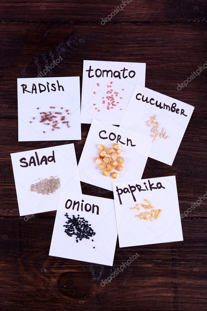 Different seeds on pieces of paper on wooden background