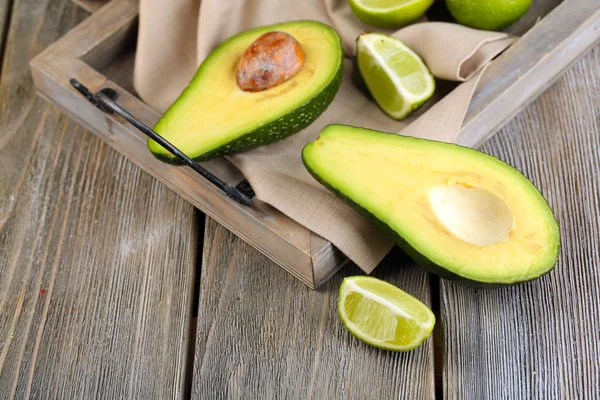 Avocado with limes on tray on wooden background — Stock Photo, Image