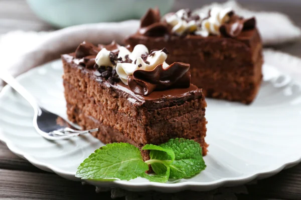 Gustosi pezzi di torta al cioccolato con menta su sfondo tavolo di legno — Foto Stock