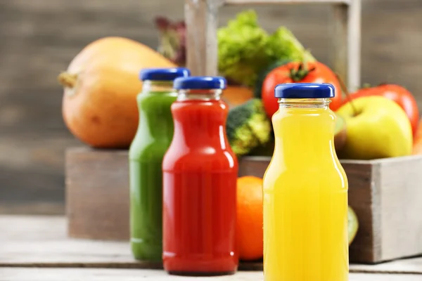 Стеклянные бутылки свежего здорового сока с набором фруктов и овощей на деревянном фоне — стоковое фото