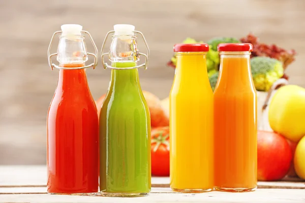 Glass bottles of fresh healthy juice with set of fruits and vegetables on wooden background — Stock Photo, Image