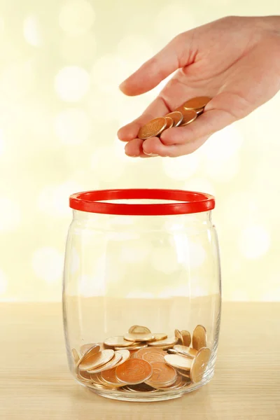 Vrouwelijke hand zetten munten in glazen fles heldere achtergrond wazig — Stockfoto