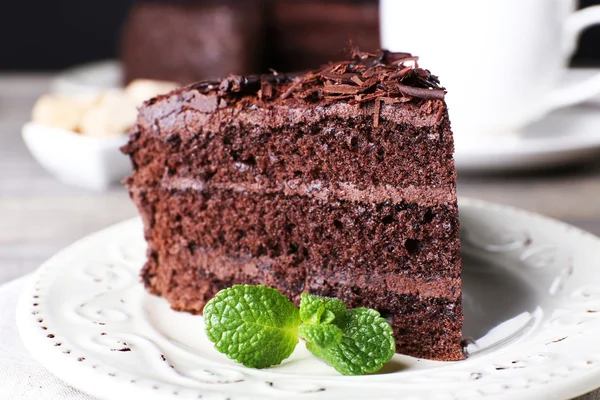 Delicioso pastel de chocolate en plato blanco con menta sobre fondo de mesa de madera, primer plano — Foto de Stock