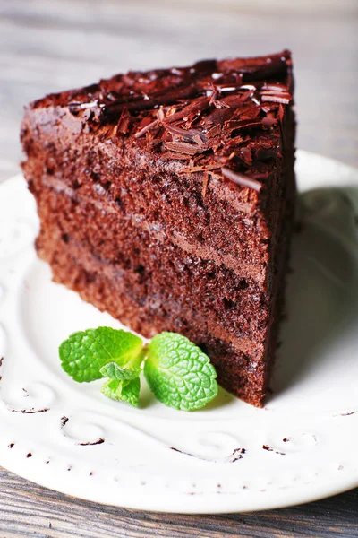 Heerlijke chocolade taart in witte plaat met munt op houten tafel achtergrond, close-up — Stockfoto