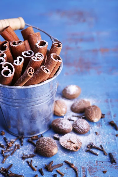 Paus de canela em balde de metal, noz-moscada e cravo na cor de fundo de mesa de madeira — Fotografia de Stock