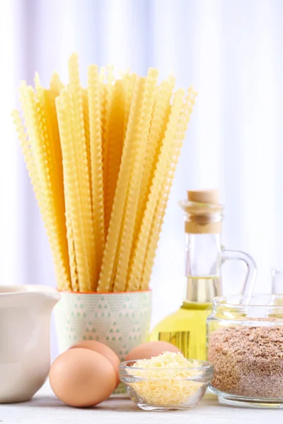 Pasta con aceite de oliva, huevos, queso y harina sobre mesa de madera sobre fondo cortina — Foto de Stock