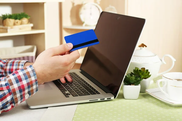 Homem segurando cartão de crédito e trabalhando no laptop em casa interior fundo — Fotografia de Stock