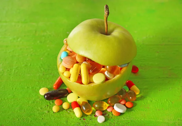 Apple and colorful pills, on color wooden background — Stock Photo, Image