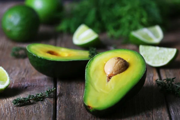 Sliced avocado with lime and herb on wooden table, closeup — Stock Photo, Image