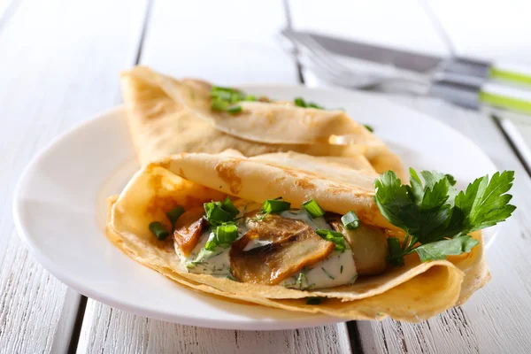 Frittelle con funghi cremosi e verdi in piatto su tavolo di legno, primo piano — Foto Stock