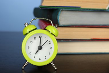 Ahşap masa ve renkli arka plan üzerinde çalar saat ile kitap yığını