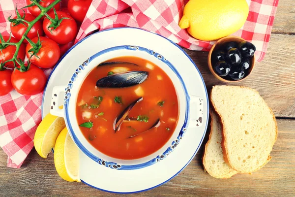 Tasty soup with mussels, tomatoes and black olives in bowl on wooden background — Stock Photo, Image