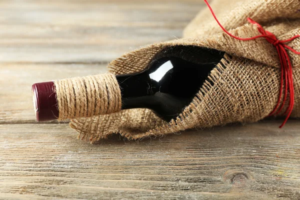 Bouteille de vin rouge enveloppée dans un tissu de toile de jute sur des planches en bois — Photo