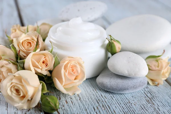 Crema cosmética con flores y piedras de spa sobre fondo de madera — Foto de Stock