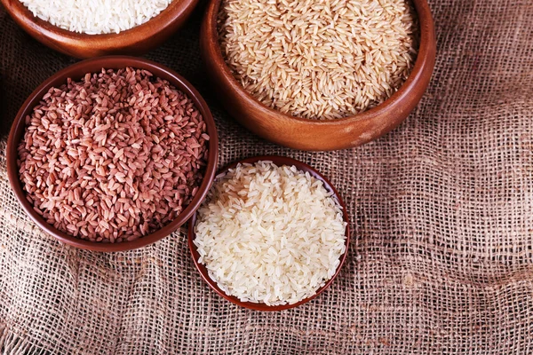 Diferentes tipos de arroz en cuencos sobre fondo de saco —  Fotos de Stock