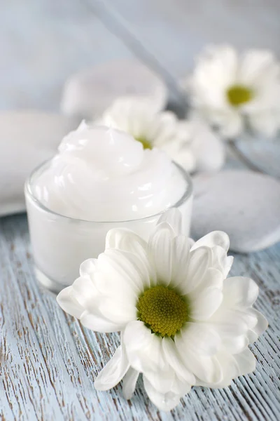 Crema cosmética con flores y piedras de spa sobre fondo de madera —  Fotos de Stock