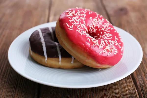 Köstliche Donuts mit Sahnehäubchen auf Teller auf Holzgrund — Stockfoto