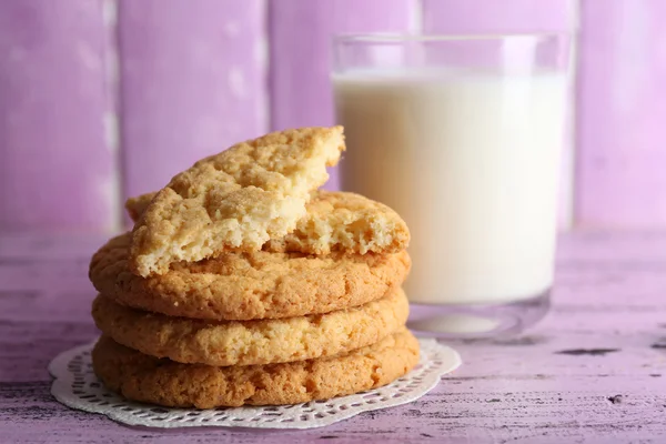 Leckere Kekse und ein Glas Milch auf farbigem Holzhintergrund — Stockfoto