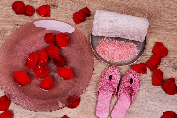 Spa bowl with water, rose petals, towel and slippers on light background. Concept of pedicure or natural spa treatment — Stock Photo, Image