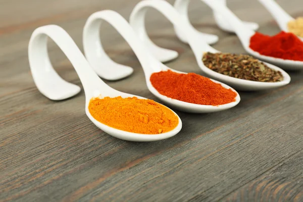 Different kinds of spices in spoons on wooden background — Stock Photo, Image