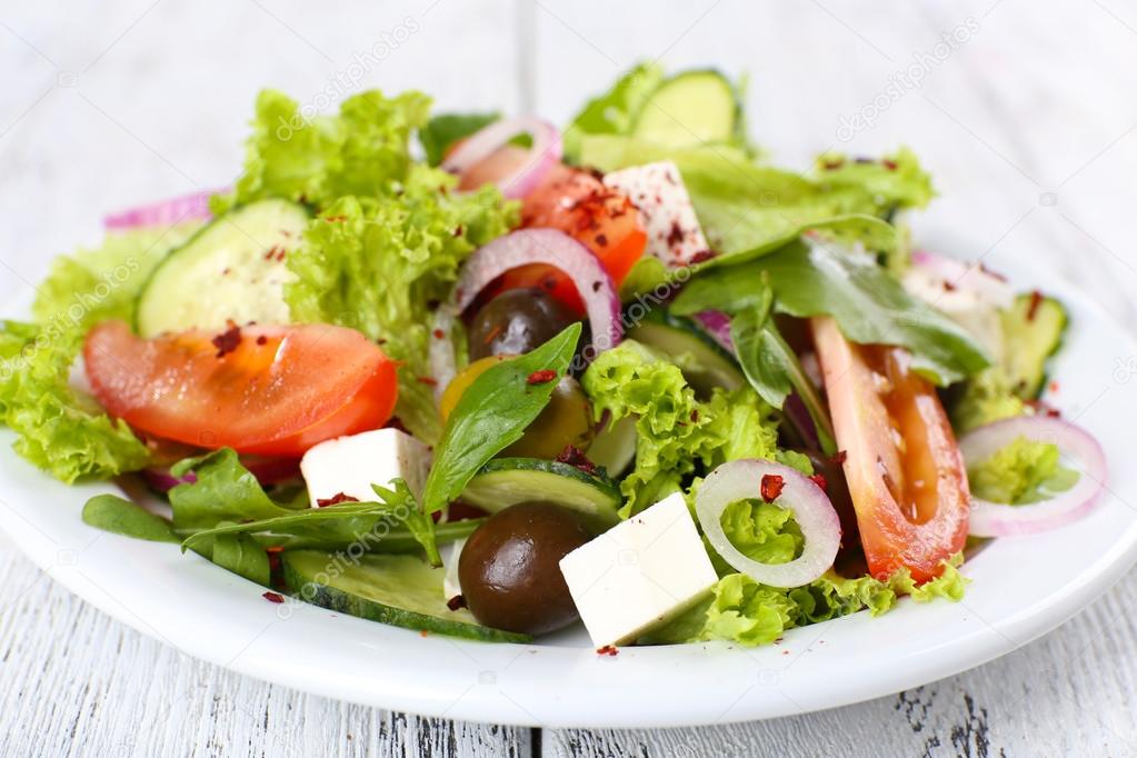 Greek salad in plate on color wooden table background