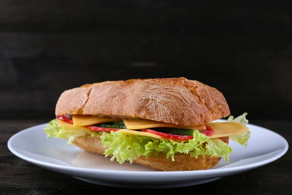 Fresh and tasty sandwich with cheese and vegetables on plate on wooden background — Stock Photo, Image