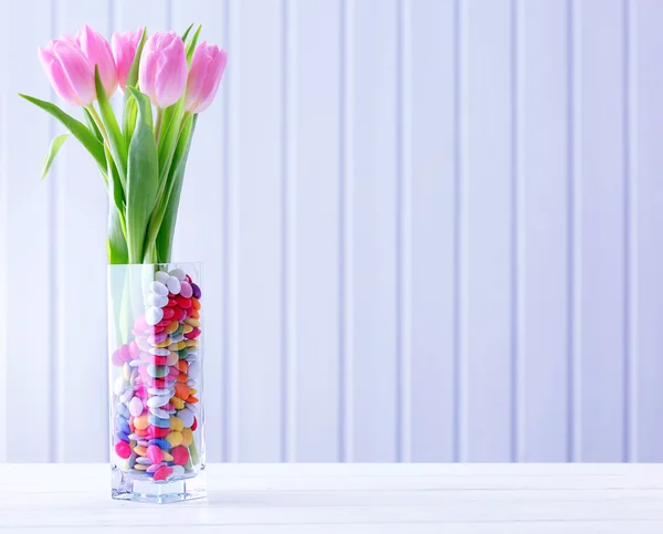 Belas tulipas cor-de-rosa com doces em vaso na mesa sobre fundo de madeira — Fotografia de Stock