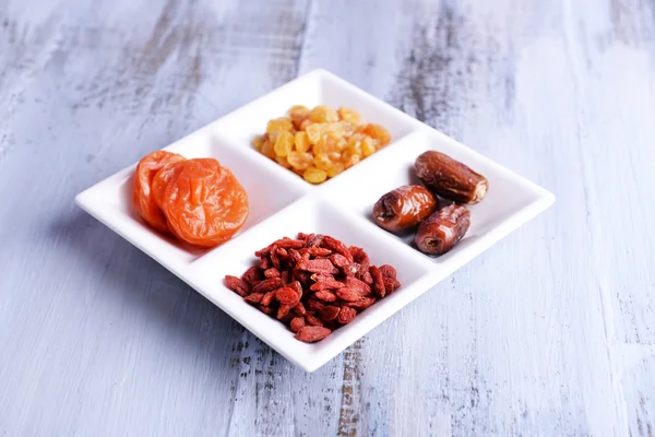 Frutos secos em placa branca na cor de fundo de mesa de madeira — Fotografia de Stock