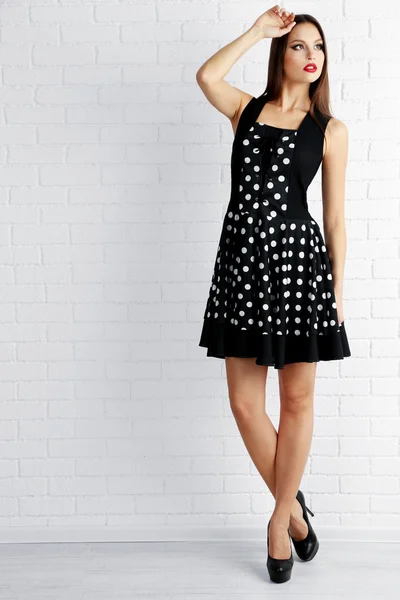 白いレンガ壁の背景に黒いドットのドレスの若い女性 — ストック写真