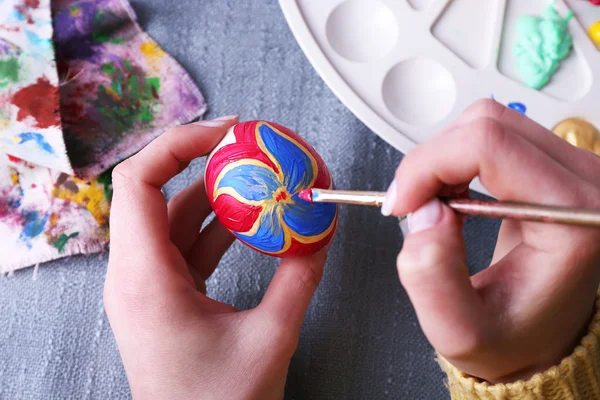 Painting Easter eggs by female hands on colorful tablecloth background — Stock Photo, Image