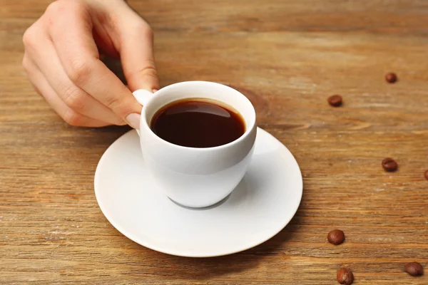 Female hand holding cup of coffee with grains on wooden background — Stock Photo, Image