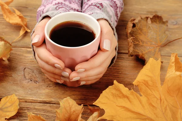 Kvinna hand innehav koppar kaffe med höstlöv på rustika träbord bakgrund — Stockfoto