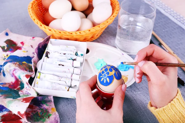 Pintura de huevos de Pascua por manos femeninas sobre fondo de mantel colorido — Foto de Stock