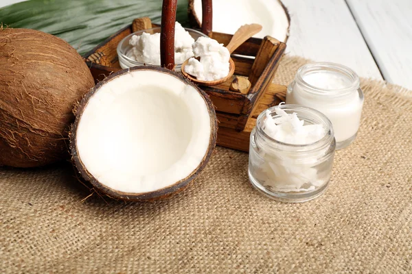 Coco con frascos de aceite de coco y crema cosmética sobre fondo de saco — Foto de Stock