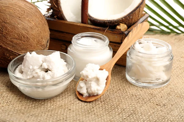 Coconut with jars of coconut oil and  cosmetic cream on sackcloth background — Stock Photo, Image